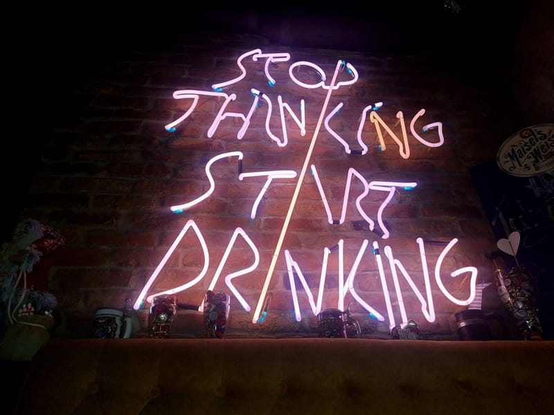 Neonski natpis „Stop thinking, start drinking“ na zidu od cigle.